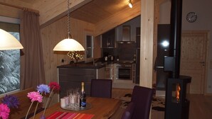 A cozy dining area with a wooden table, purple chairs, and a vase of flowers. A kitchen with modern appliances is visible in the background. - Chalet Royal with in-house wellness and large living room, large new balcony #23 (Turrach)
