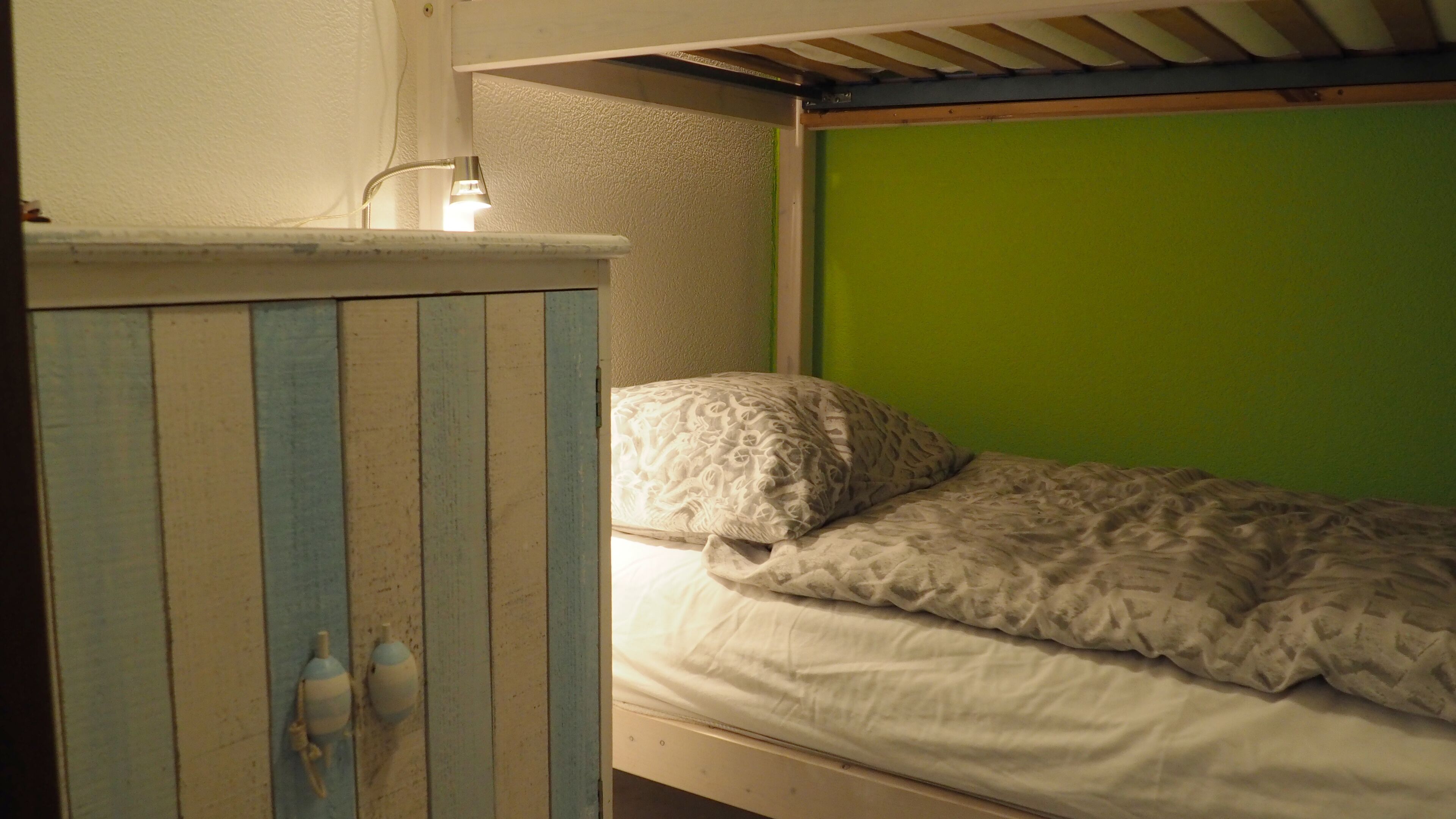 A bunk bed with a green wall and a wooden headboard.