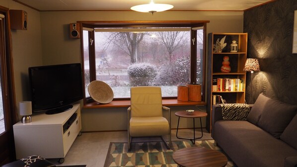 A living room with a television, a chair, a sofa, a small table, and a bookshelf.