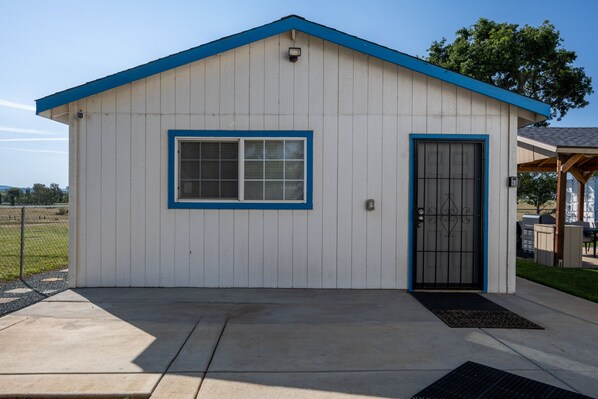 A small, single-story building with a blue roof and white walls, featuring a single door and a window with a blue frame.