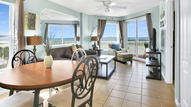 A spacious living area with a dining table, chairs, a sofa, and a balcony with a view of the beach.