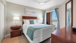 A hotel room with a bed, bedside tables, a desk, a ceiling fan, and a view of the outdoors. - Surf Beach 506 - Spectacular Sunsets - Beach Front (Treasure Island)