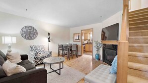 A living room with a sofa, patterned armchair, round coffee table, and a TV. There's a staircase to the right and a kitchen in the background. - Near Beaches Town & Shopping (Naples)