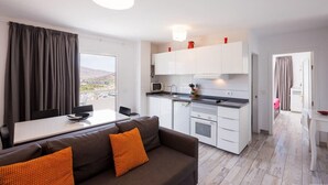 Une cuisine moderne avec des meubles blancs, un coin repas comprenant une table et des chaises, et un canapé agrémenté de coussins orange.