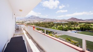 Un balcon offrant une vue sur un paysage montagneux, un terrain de sport et un bâtiment situé au loin.