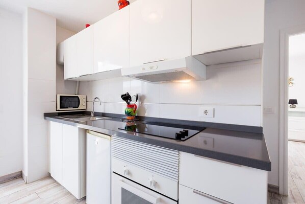 Una cocina moderna con armarios blancos, encimera negra y un microondas.