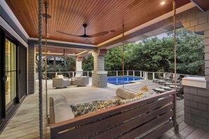 A covered outdoor area with a pool, seating, and a ceiling fan.