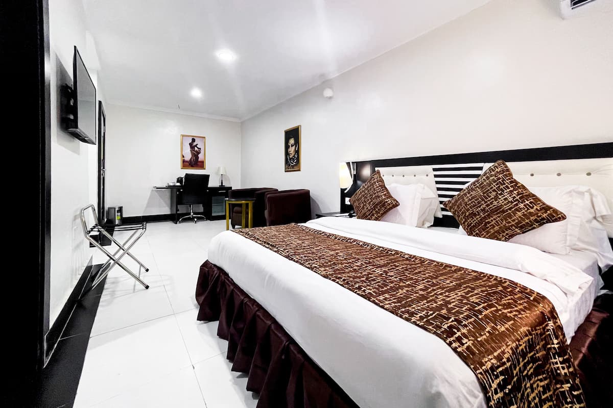 A hotel room with a large bed, a desk, a chair, and a TV.