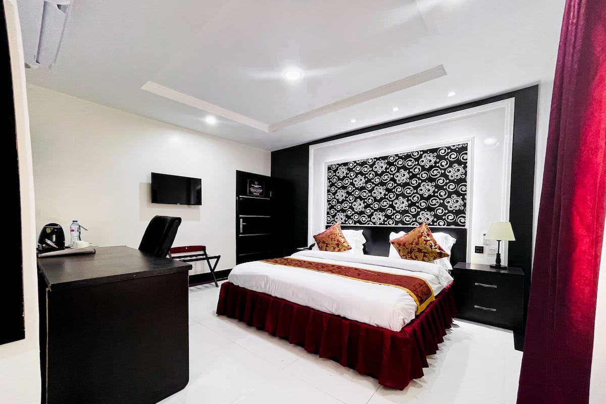 A modern hotel room with a large bed, a desk, a TV, and a wardrobe.