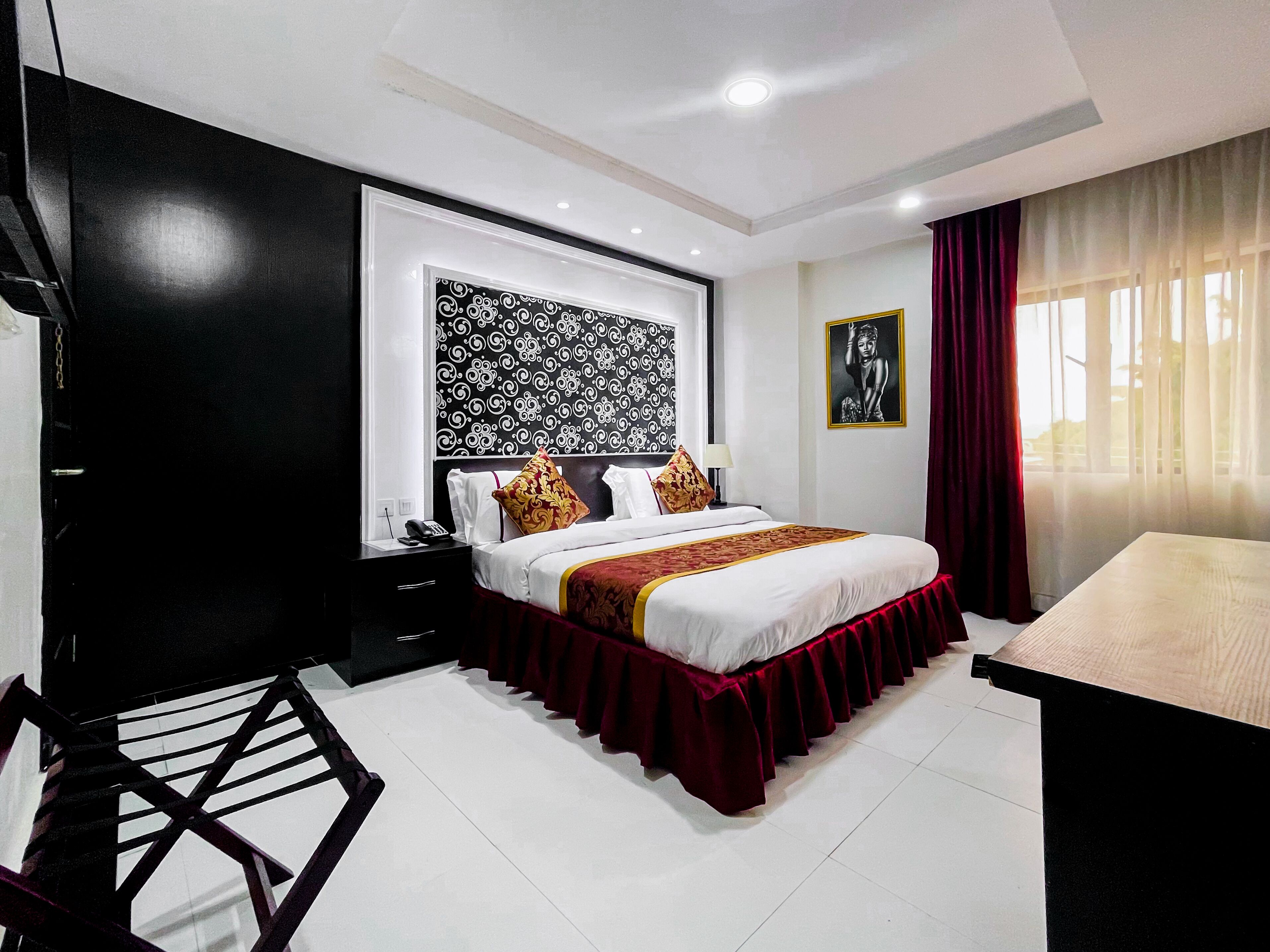 A hotel room with a large bed, a desk, a chair, a nightstand, and a patterned wall.
