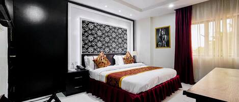 A hotel room with a large bed, a desk, a chair, a nightstand, and a patterned wall.