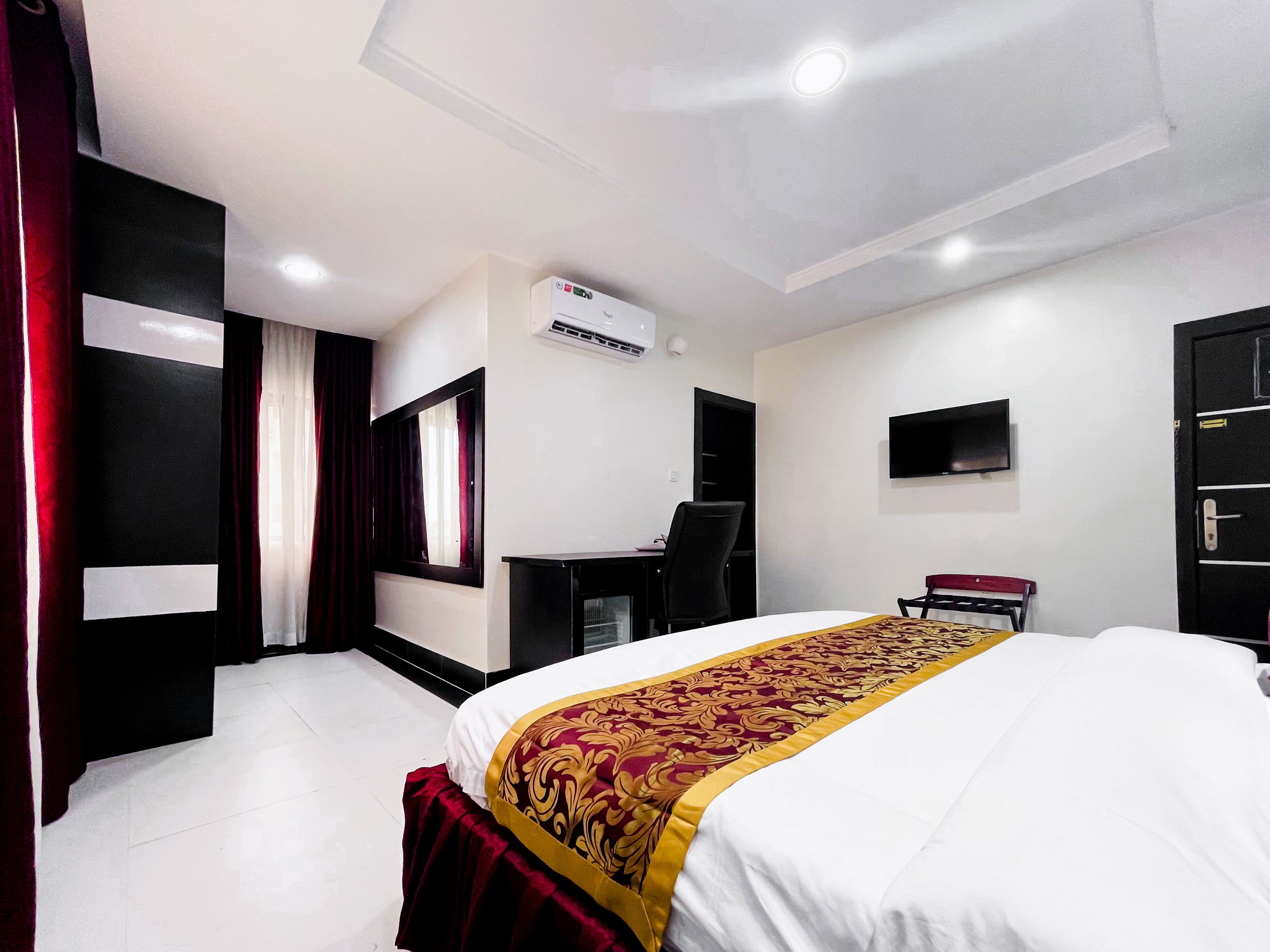 A hotel room with a bed, a desk, a chair, a TV, and an air conditioning unit.