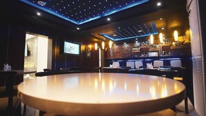 A modern bar area with a large round table, seating, and a projection screen. - Pasadena Suites (Lekki)