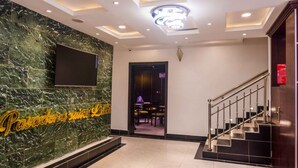 A hotel lobby with a marble wall, a staircase, and a reception area. - Pasadena Suites (Lekki)