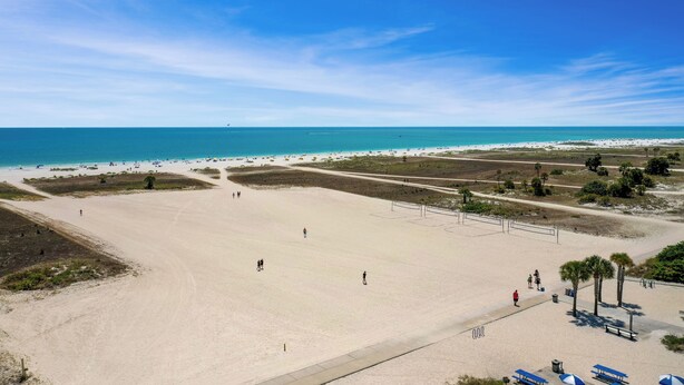 A wide sandy beach with a clear view of the ocean, a few people walking, and a few beach umbrellas.