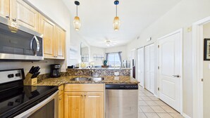 A kitchen with a microwave, stove, coffee maker, and dishwasher. There are wooden cabinets and a granite countertop.