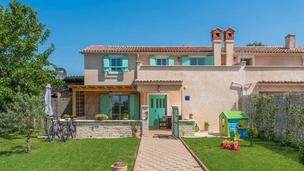 Una casa a due piani con un vialetto lastricato che conduce all'ingresso, un'area giochi e una bicicletta parcheggiata fuori.
