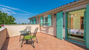 Una terrazza con tavolo e sedie, un letto con porta aperta e vista sul cielo.