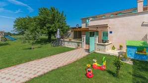 Una casa con vialetto in pietra, giardino e area giochi con giochi.