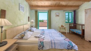 Camera da letto con soffitto in legno, un letto con copripiumino decorato, un comodino con una lampada e vista all'esterno da una finestra.