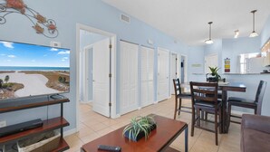 A living room with a TV, a dining area with chairs, and a kitchen in the background.