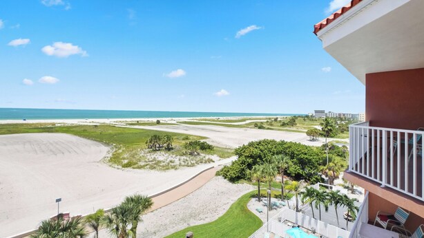 Blick auf den Strand vom Balkon aus, mit Pool und Liegestühlen.