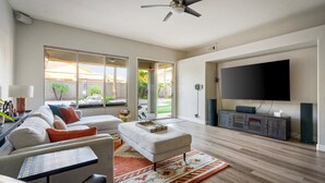 A spacious living room with a large TV, a ceiling fan, and a view of the outdoors through large sliding glass doors. - Relax in Paradise - 4 Bed + 2 Bath w/ Gorgeous Heated Private Pool & Spa! (Peoria)