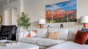 A modern living room with a sectional sofa, a black leather armchair, and a large wall-mounted painting of a desert landscape. - Relax in Paradise - 4 Bed + 2 Bath w/ Gorgeous Heated Private Pool & Spa! (Peoria)