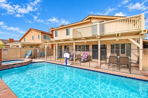 A residential swimming pool with a covered patio area, a basketball hoop, and outdoor seating.