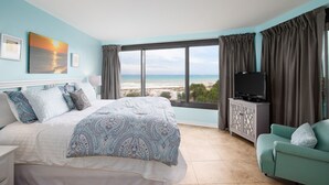 Ein Schlafzimmer mit einem großen Bett, einem Fernseher auf einem Schrank und Blick auf den Strand.