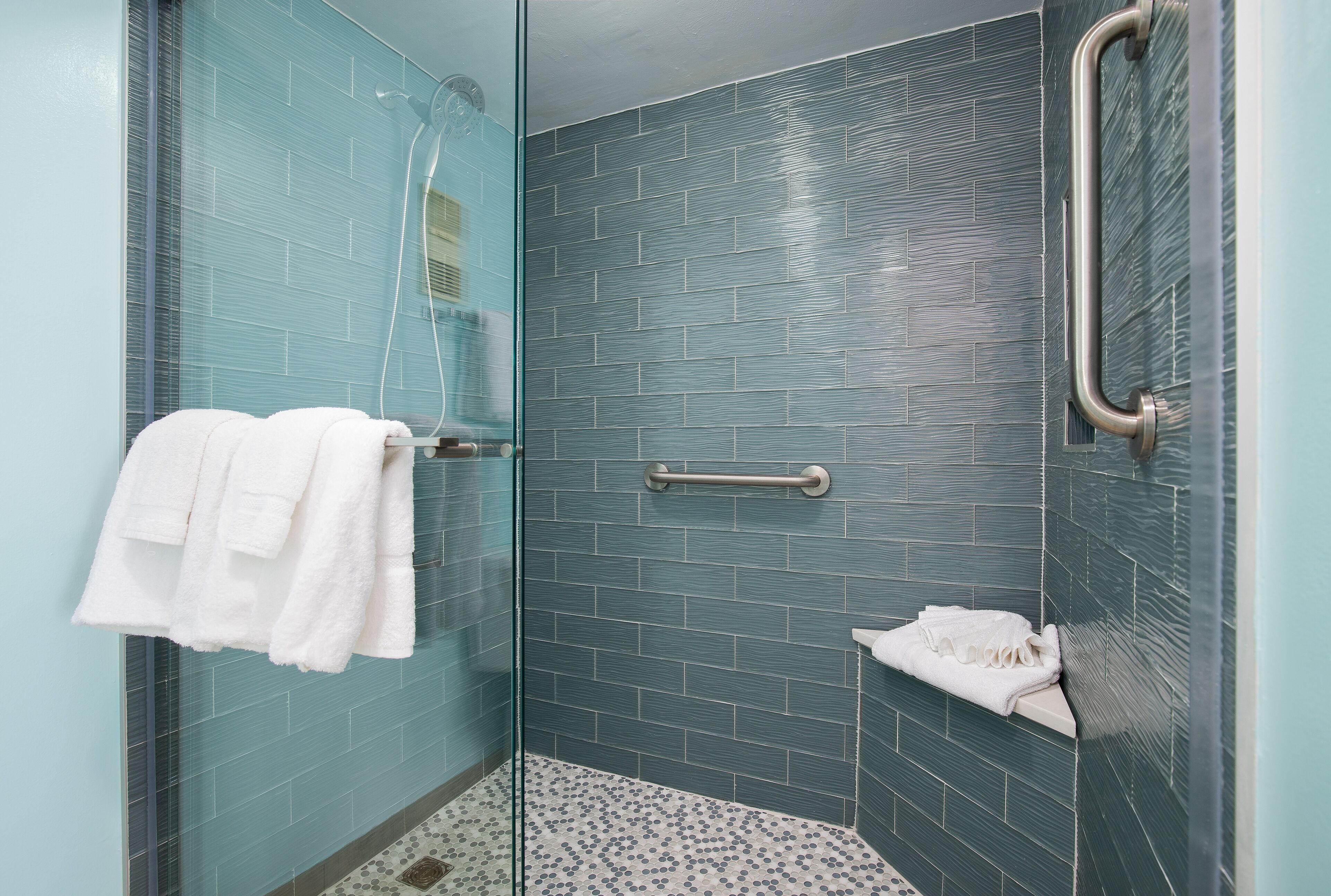 A shower with a glass door, a handrail, and a tiled wall.