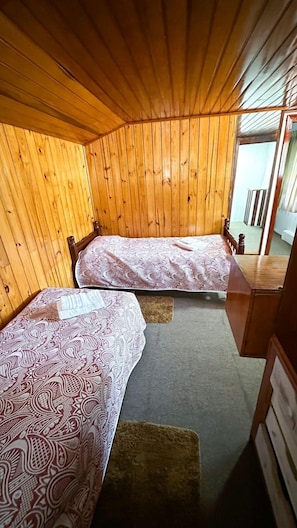 Una cabaña con dos literas de madera, un pequeño escritorio de madera y una ventana con cortinas.