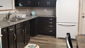 A kitchen with dark cabinets, a white refrigerator, a granite countertop, and a wooden floor. - La Casita Guest House (Muscatine)