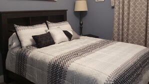 A bedroom with a bed, a nightstand, a lamp, a ceiling fan, and a painting on the wall. - La Casita Guest House (Muscatine)