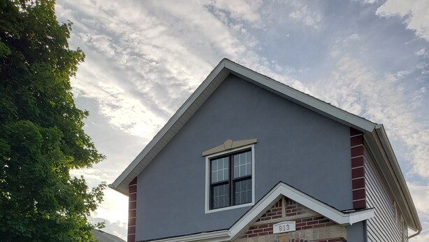 A two-story house with a grey exterior, a brick archway entrance, and a front porch. - La Casita Guest House (Muscatine)