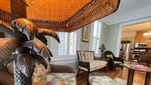 A living room with wicker furniture, a glass coffee table, and a view into the kitchen. - The Gregory House, A Southern Tropical Get Away! (Pensacola)