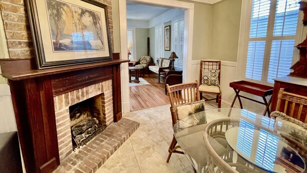 A living room with a fireplace, a glass table, and a view of the adjacent dining area. - The Gregory House, A Southern Tropical Get Away! (Pensacola)
