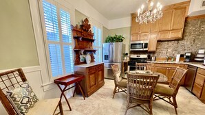 A kitchen with wooden cabinets, a dining table with chairs, a chandelier, and a refrigerator. - The Gregory House, A Southern Tropical Get Away! (Pensacola)