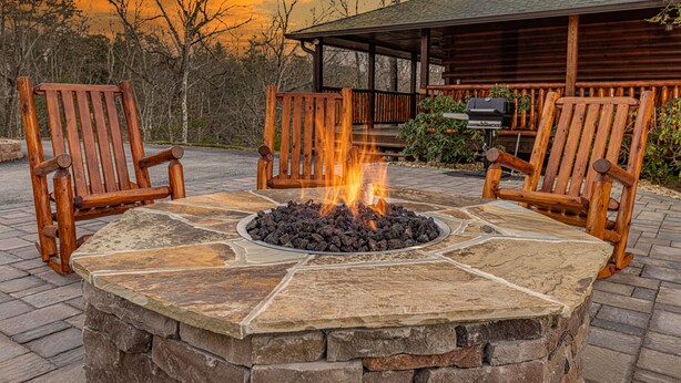 A stone fire pit with two wooden Adirondack chairs, a wooden deck, and a cabin in the background. - Comfort & Relaxation 3 br Cabin Wraparound Decks Amazing Views 2 Hot Tubs (Pigeon Forge)