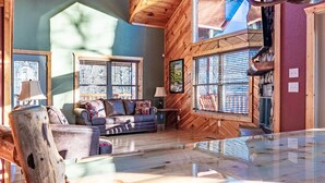 A spacious living area with a large glass-top table, wooden furniture, and a prominent antler chandelier. - Comfort & Relaxation 3 br Cabin Wraparound Decks Amazing Views 2 Hot Tubs (Pigeon Forge)