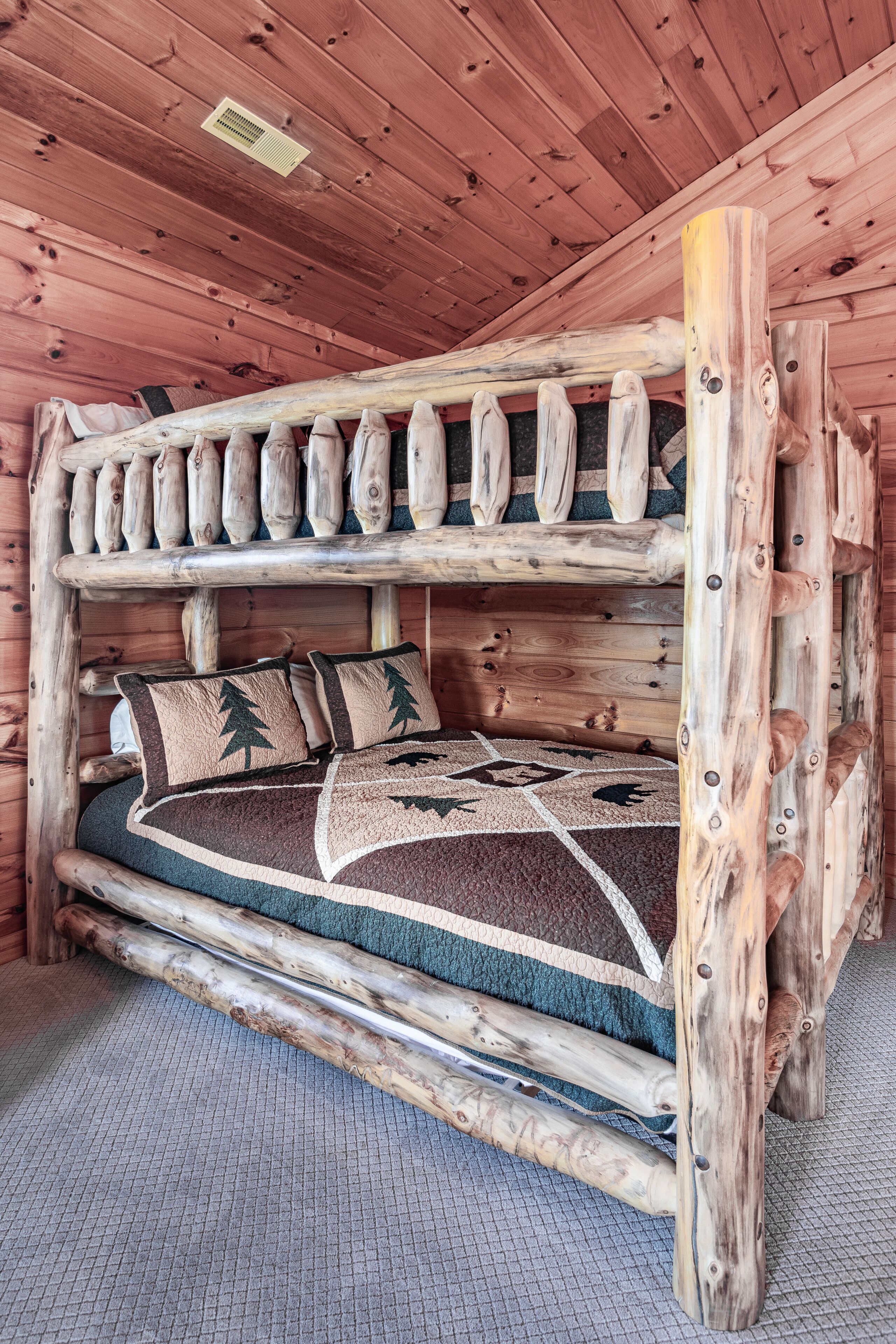 A bunk bed with a wooden frame and a blanket with a tree design.