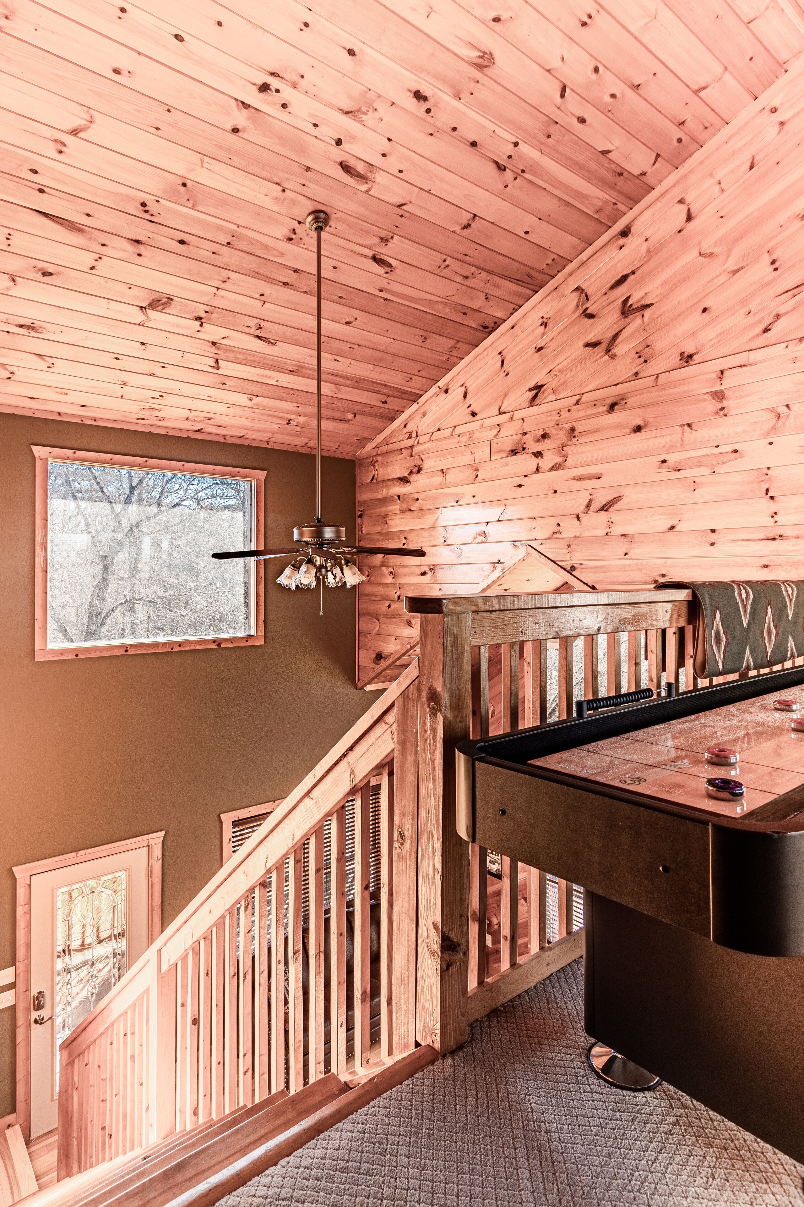 A wooden interior with a staircase, a ceiling fan, a window, and a pool table.