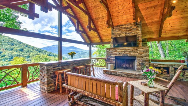 Una terraza de madera con una chimenea de piedra, bancos de madera y vistas a las montañas.