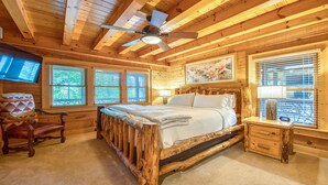 Un dormitorio de cabaña de madera con una cama, una silla, una mesita de noche y un ventilador de techo.