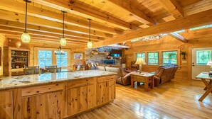 Interior de una cabaña de madera espaciosa con una isla de cocina grande, asientos de cuero y múltiples ventanas que ofrecen luz natural.