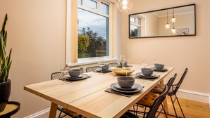 Un comedor con una larga mesa de madera dispuesta para cuatro, sillas negras y un amplio ventanal con vistas a árboles.