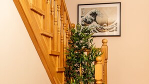 Una escalera de madera con un banco blanco al pie, una planta en maceta a un lado y una obra de arte enmarcada en la pared.