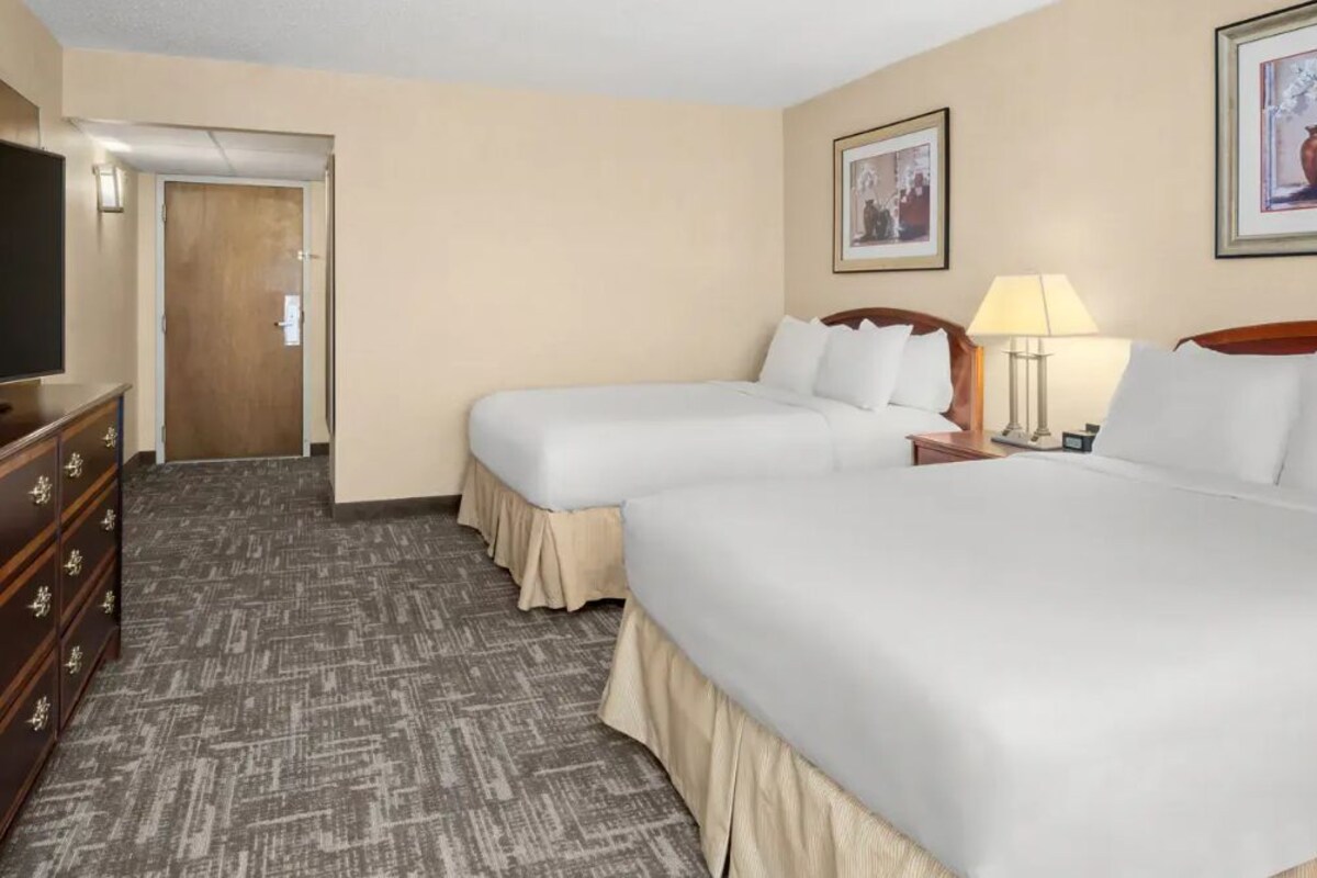 A hotel room with two beds, a dresser, a television, and framed artwork on the walls.