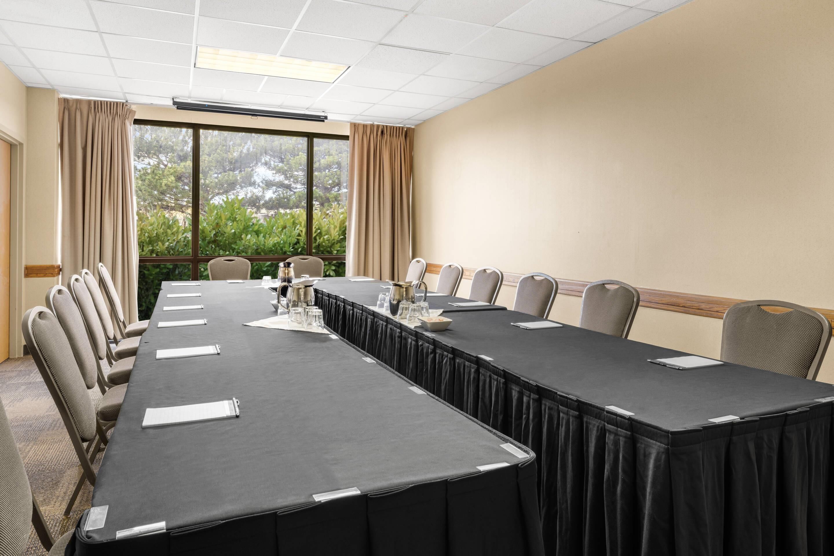 A conference room with a long table, chairs, and a view through large windows.