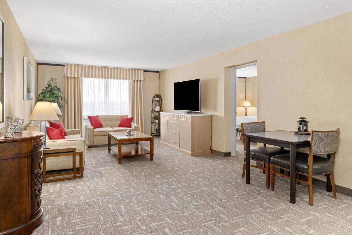 Habitación de hotel con sala de estar, mesa de comedor, televisor y aparador.